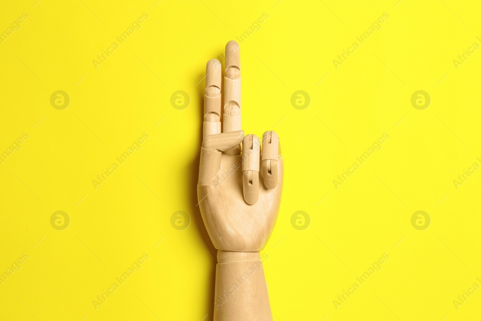 Photo of Wooden mannequin hand on yellow background, top view