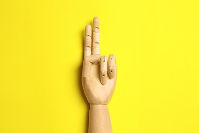 Wooden mannequin hand on yellow background, top view