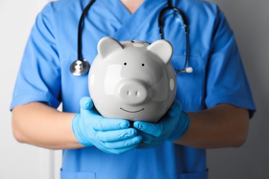 Photo of Doctor holding piggy bank on white background, closeup. Medical insurance