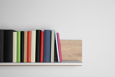 Different books on wooden shelf near white wall, space for text