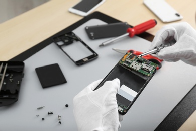 Photo of Technician repairing broken smartphone at table, closeup