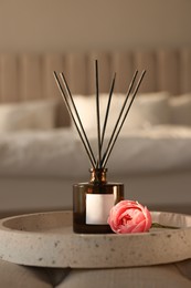 Photo of Aromatic reed air freshener and flower on bench in bedroom