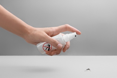 Image of Woman spraying insect repellent on mosquito against grey background, closeup