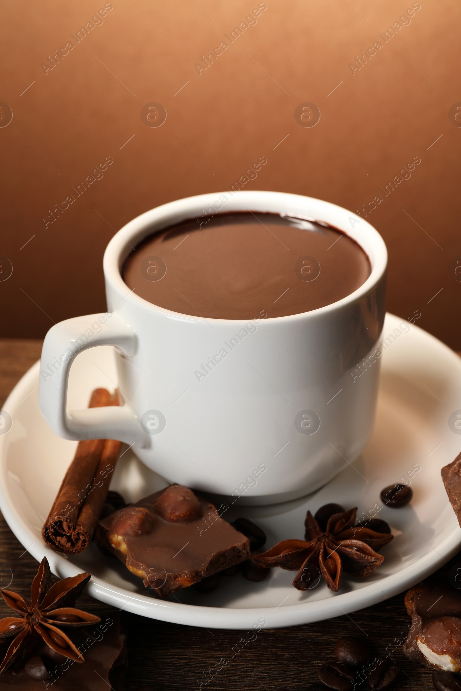 Photo of Cup of delicious hot chocolate, spices and coffee beans on wooden table