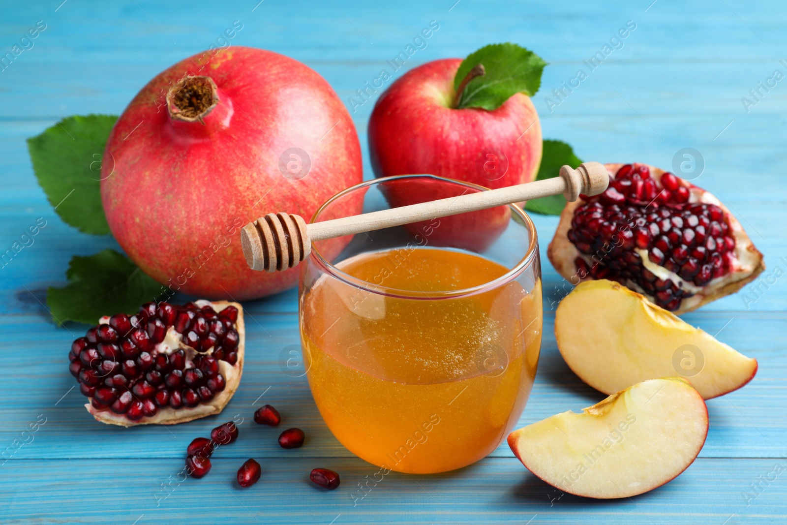 Photo of Honey, pomegranate and apples on light blue wooden table, closeup. Rosh Hashana holiday