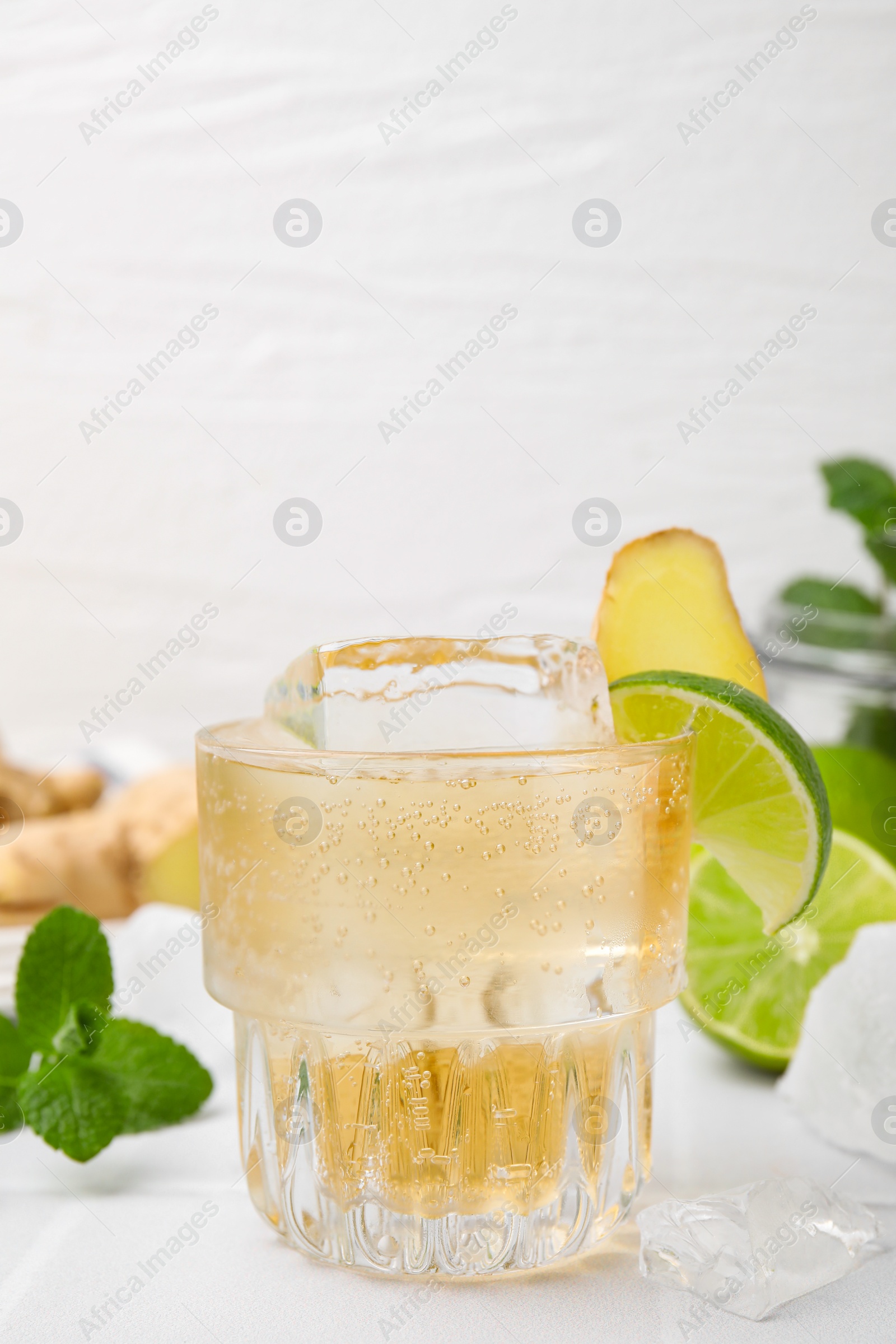 Photo of Glass of tasty ginger ale with ice cube and ingredients on white table, closeup