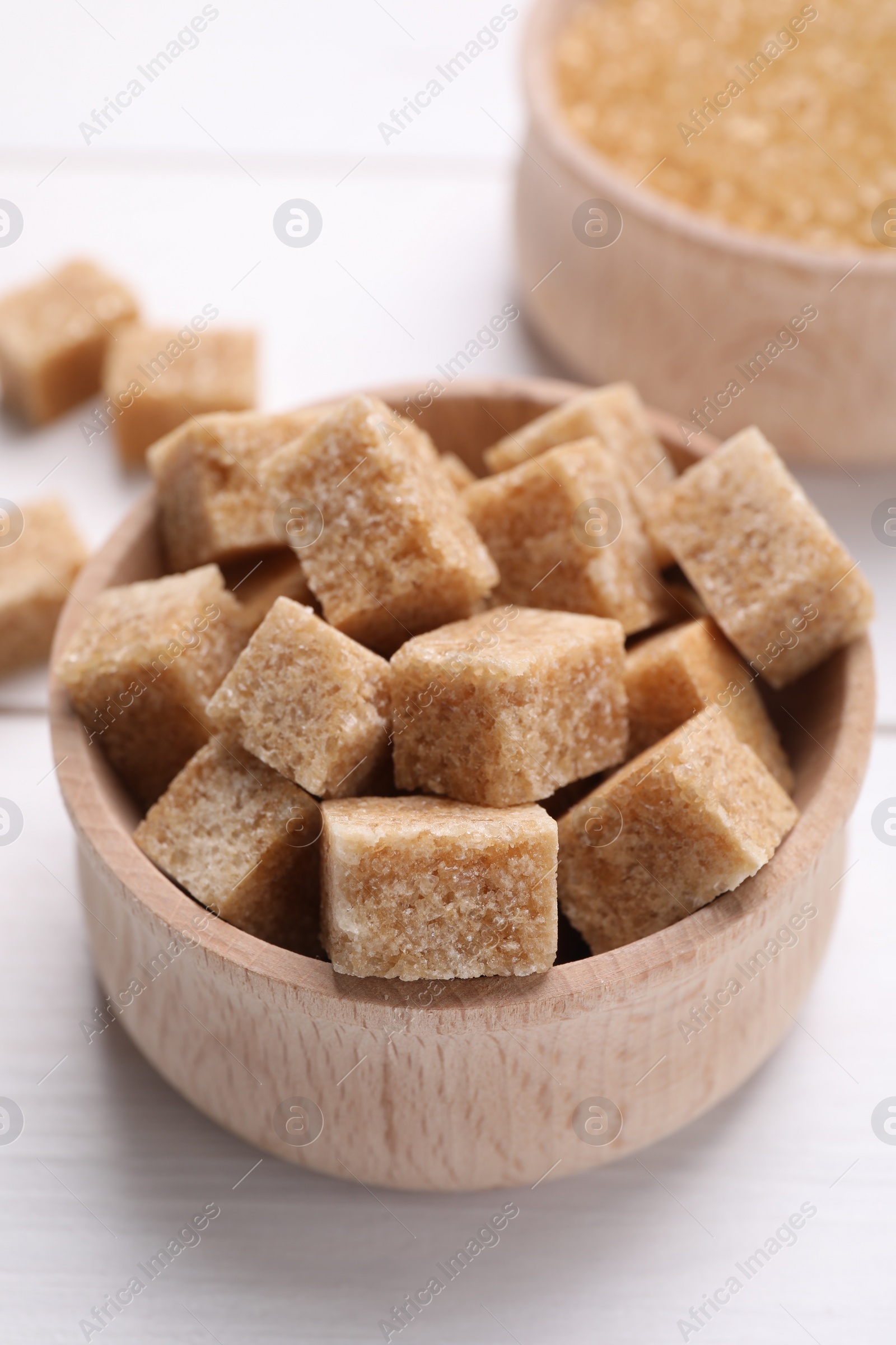 Photo of Brown sugar cubes in bowl on white table, closeup