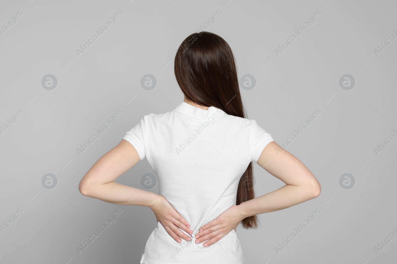 Photo of Woman suffering from back pain on light grey background. Arthritis symptoms