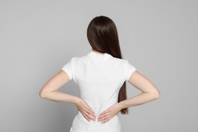 Woman suffering from back pain on light grey background. Arthritis symptoms