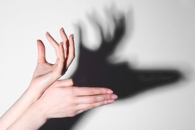Shadow puppet. Woman making hand gesture like deer on light background, closeup