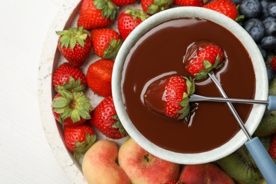 Photo of Dipping strawberries into fondue pot with chocolate on white table, top view