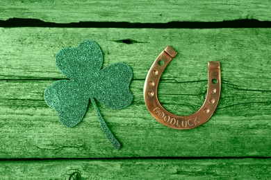 Image of St. Patrick's day. Decorative clover leaf and golden horseshoe on green wooden background, flat lay