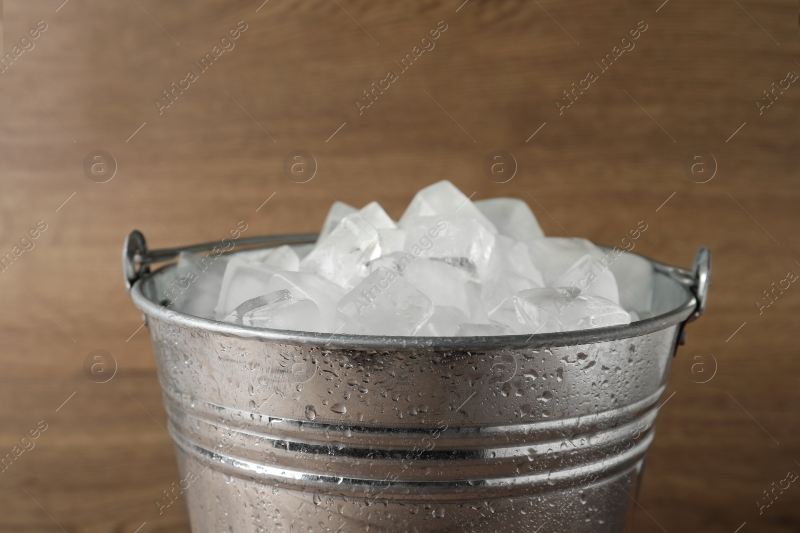 Photo of Metal bucket with ice cubes on wooden background