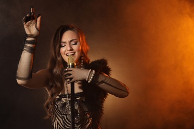 Photo of Beautiful young woman with microphone singing in color lights and smoke, space for text