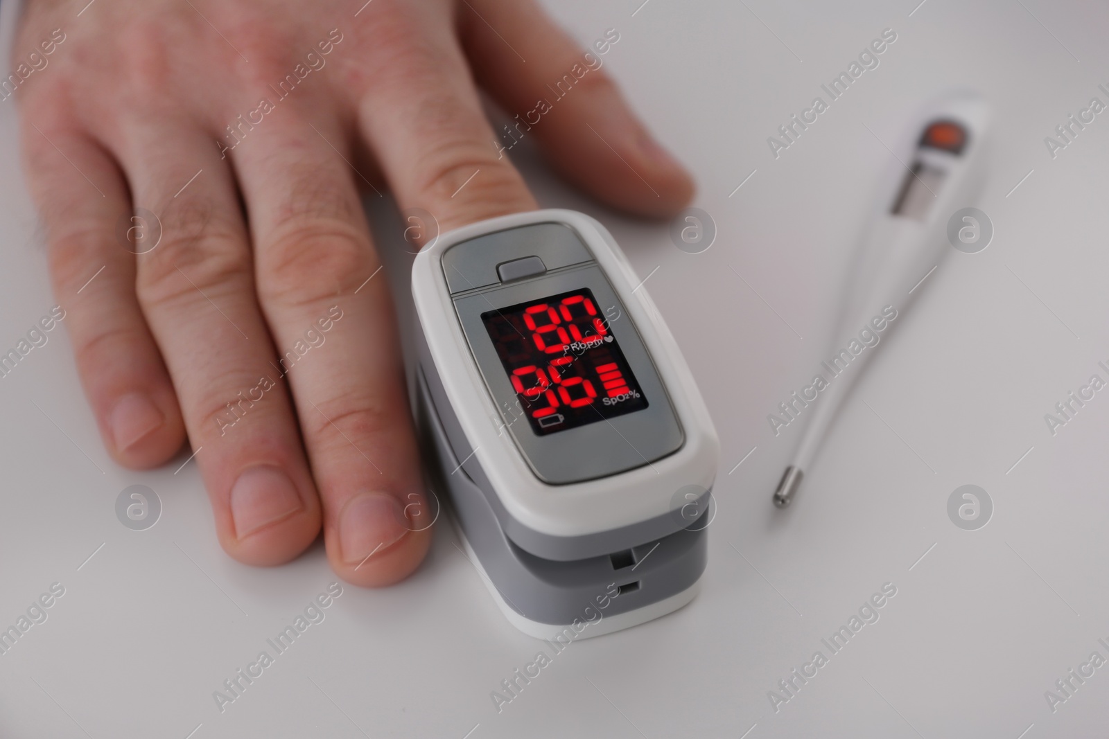 Photo of Man measuring oxygen level with modern fingertip pulse oximeter at white table, closeup