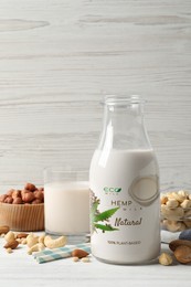 Glass and bottle of hemp milk and different nuts on white wooden table. Vegan product