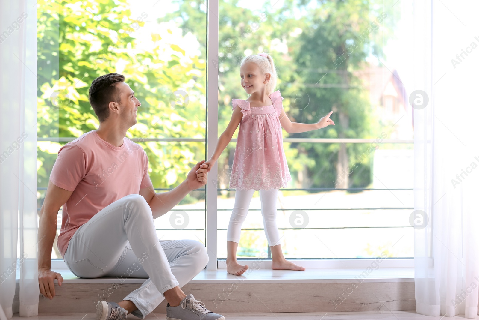 Photo of Young man with cute little girl near window at home