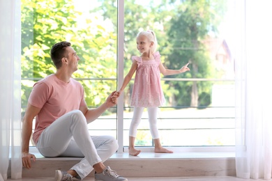 Photo of Young man with cute little girl near window at home