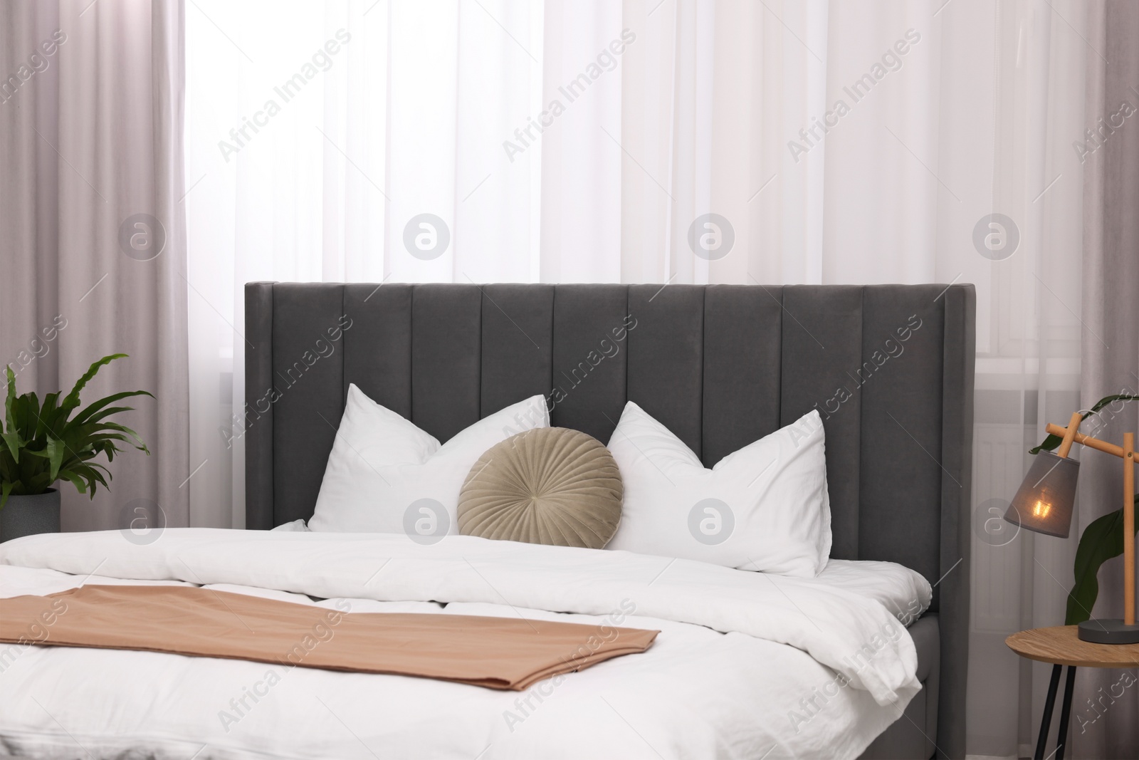 Photo of Stylish bedroom interior with large bed, lamp and houseplant