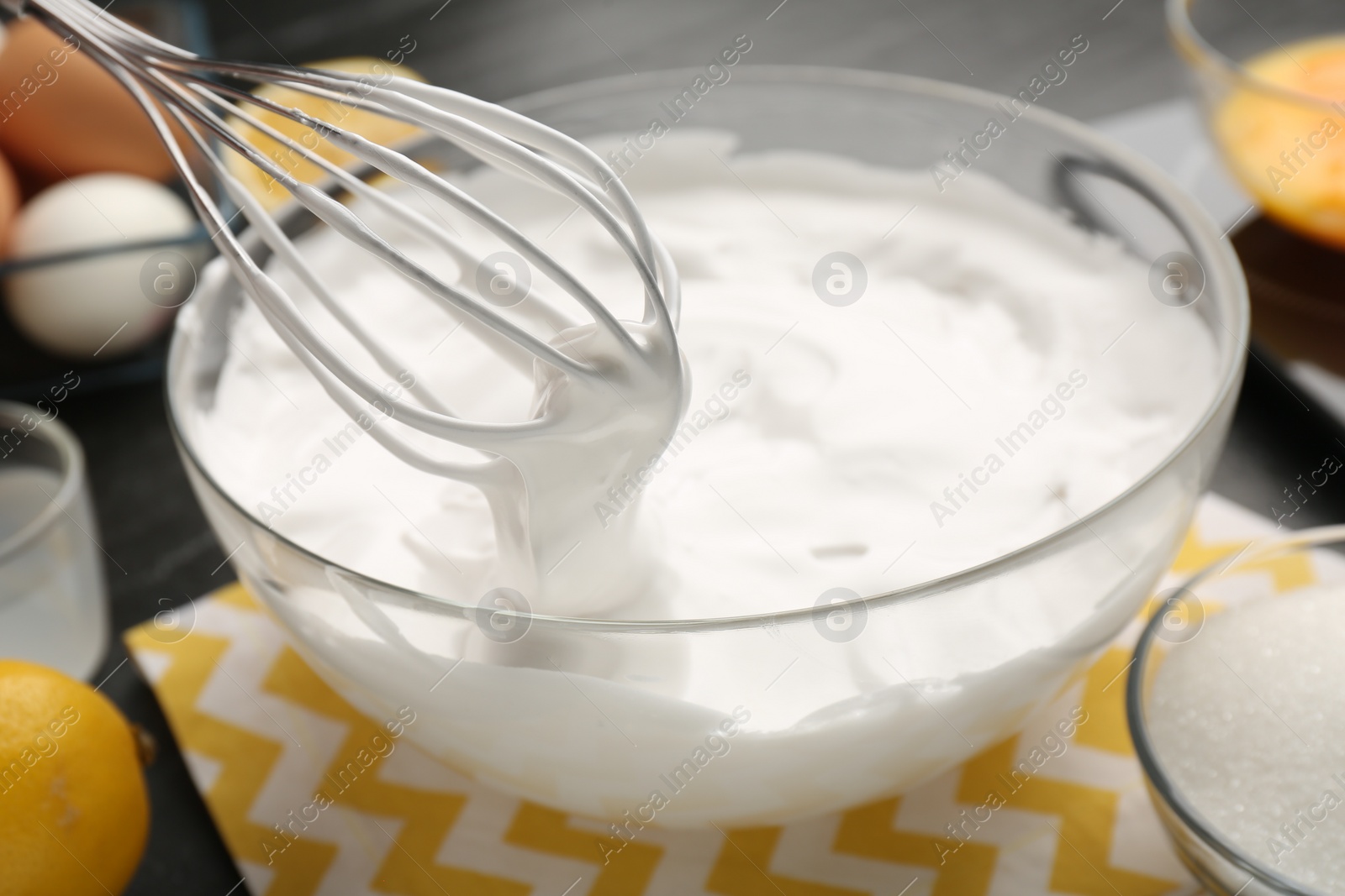 Photo of Bowl with whipped cream, whisk and ingredients on table, closeup