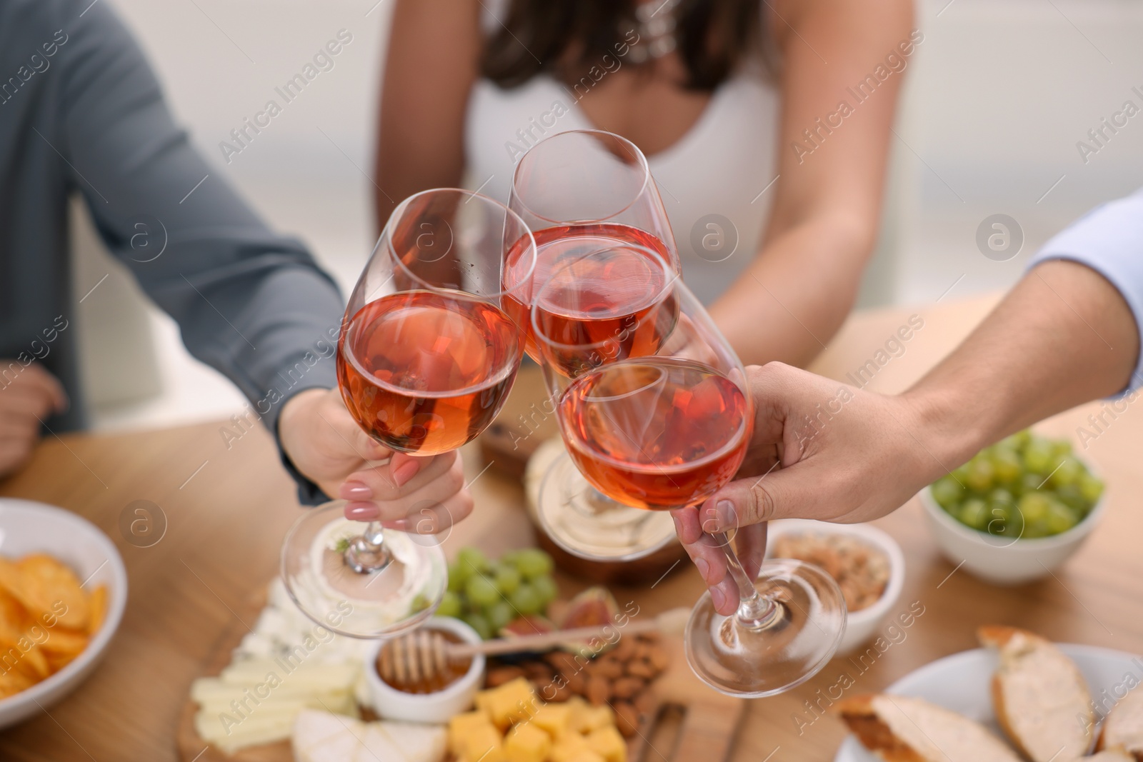 Photo of People clinking glasses with rose wine above wooden table indoors, closeup