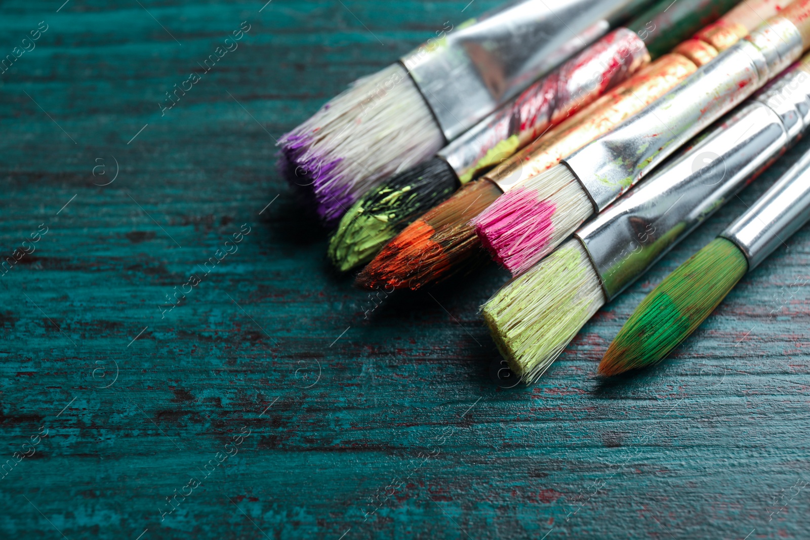 Photo of Different paint brushes on wooden table, closeup. Space for text