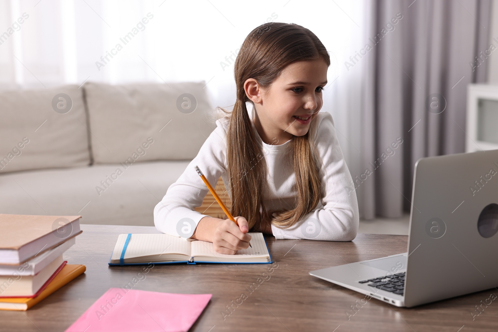 Photo of E-learning. Cute girl taking notes during online lesson at table indoors