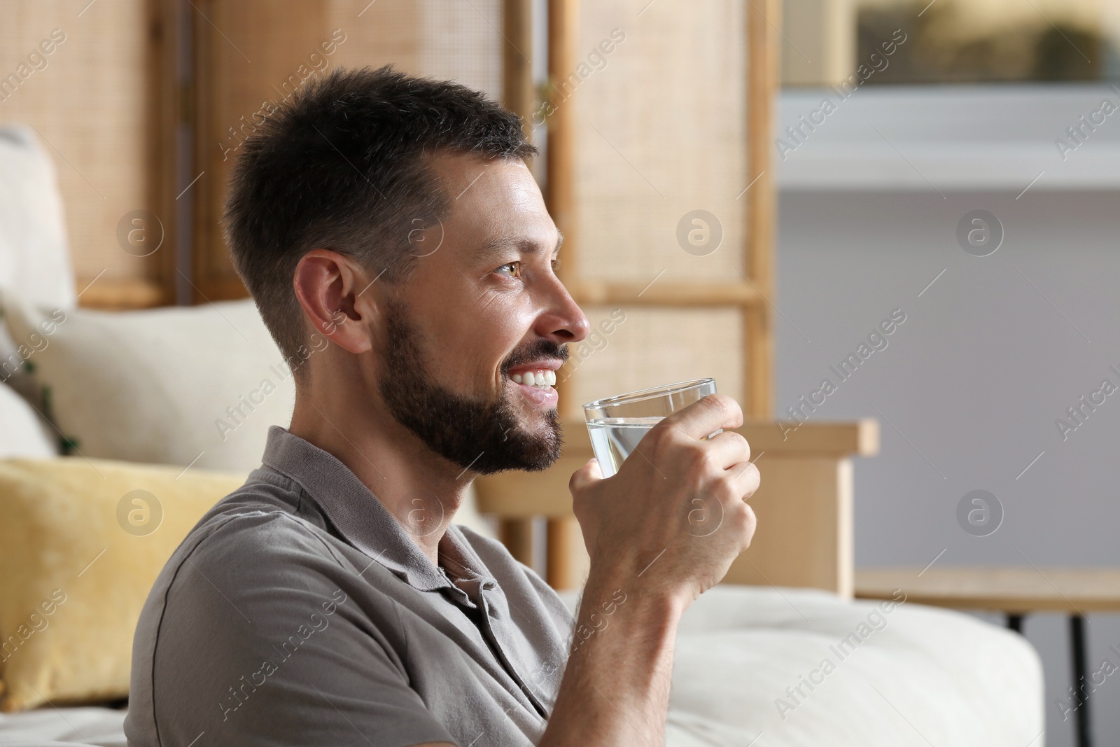 Photo of Happy man drinking water indoors. Refreshing drink