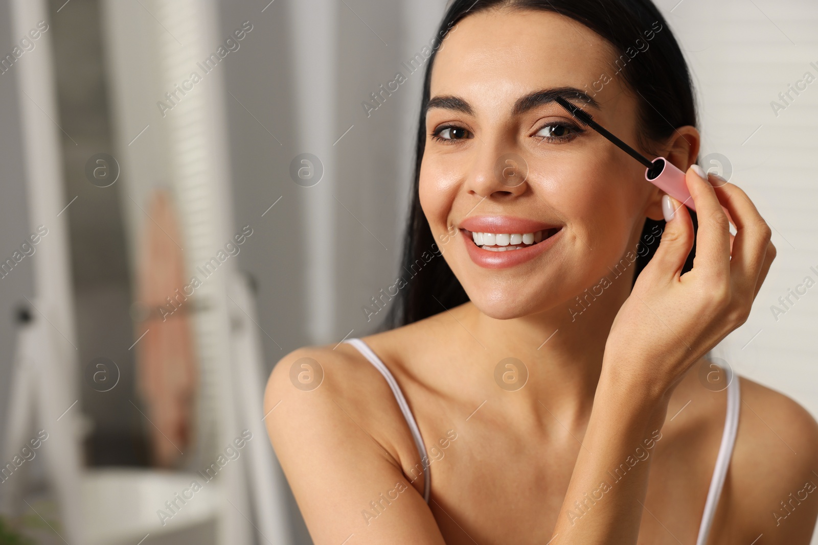 Photo of Beautiful young woman applying mascara indoors, closeup. Space for text