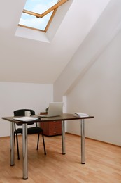 Photo of Stylish workplace with laptop and documents in attic room. Interior design