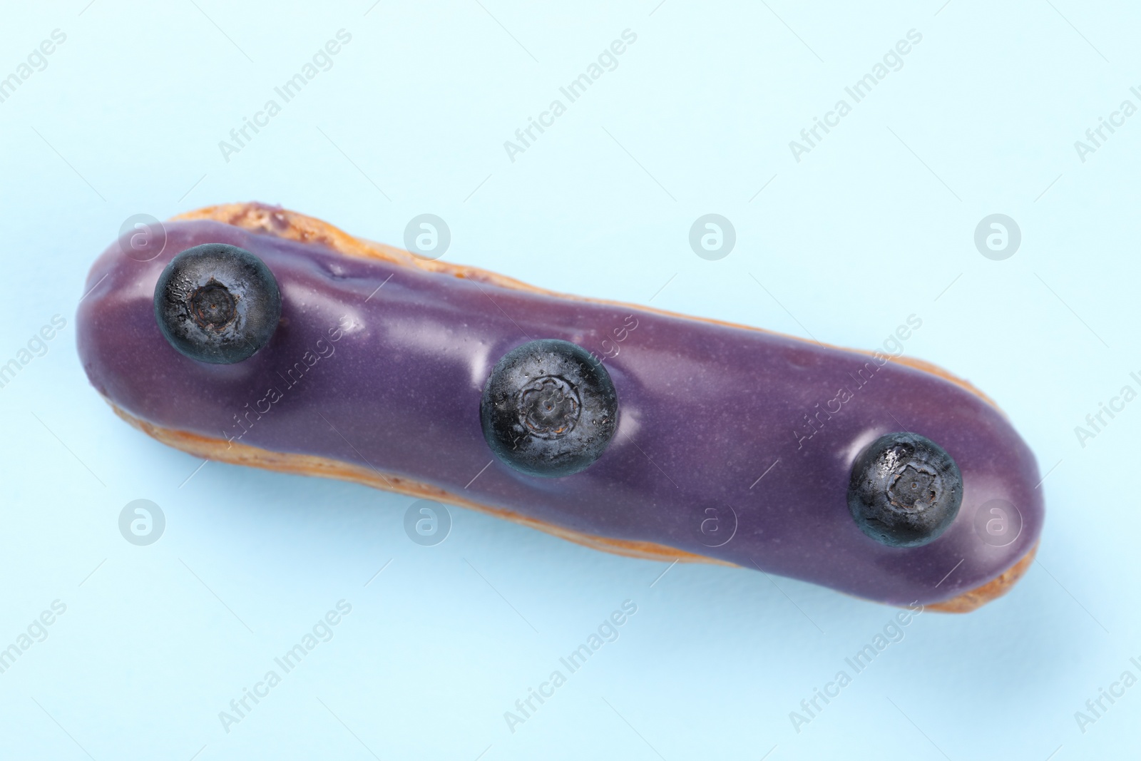 Photo of Delicious eclair covered with glaze on light blue background, top view