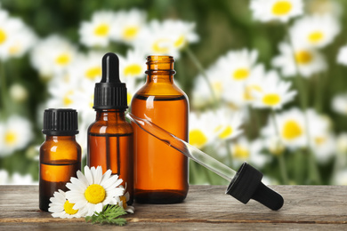 Bottles of essential oil and chamomile flowers on wooden table against blurred background