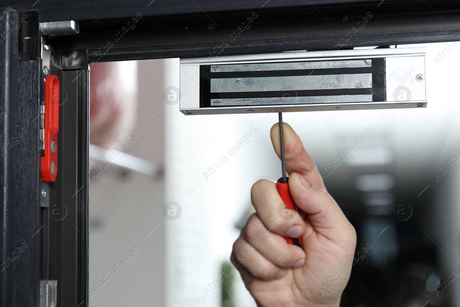 Photo of Man with screwdriver installing electromagnetic door lock indoors, closeup. Home security