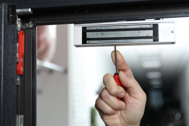 Man with screwdriver installing electromagnetic door lock indoors, closeup. Home security