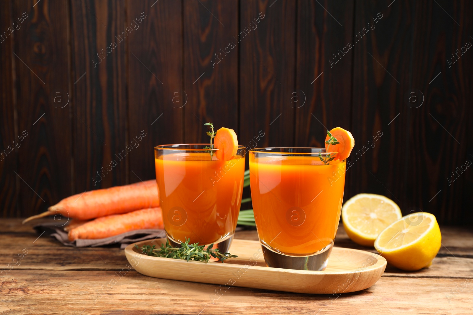 Photo of Glasses of tasty carrot juice and ingredients on wooden table