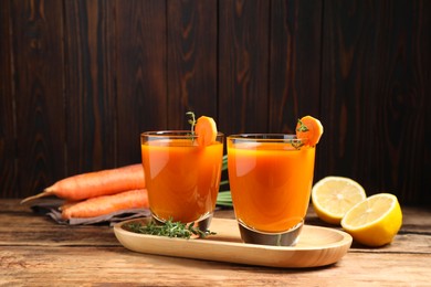 Glasses of tasty carrot juice and ingredients on wooden table