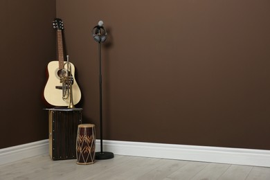Acoustic guitar, trumpet, hand drum and microphone near brown wall indoors, space for text. Musical instruments