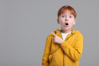 Surprised little boy pointing at something on grey background, space for text