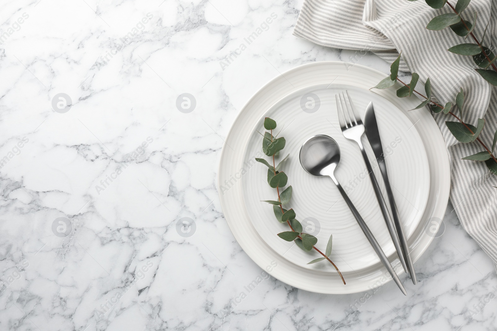 Photo of Stylish setting with cutlery, napkin, eucalyptus branches and plates on white marble table, top view. Space for text