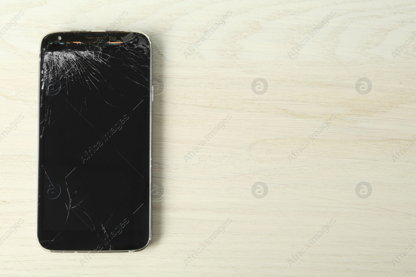 Photo of Top view of smartphone with cracked screen on white wooden table, space for text. Device repair
