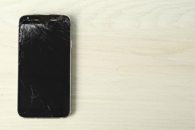 Photo of Top view of smartphone with cracked screen on white wooden table, space for text. Device repair