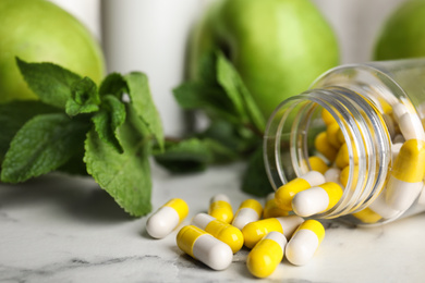 Photo of Bottle with vitamin pills, apples and mint on white marble table, closeup