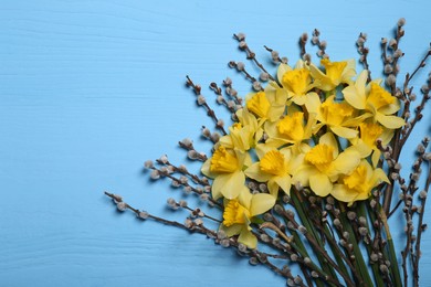Bouquet of beautiful yellow daffodils and willow flowers on light blue wooden table, top view. Space for text
