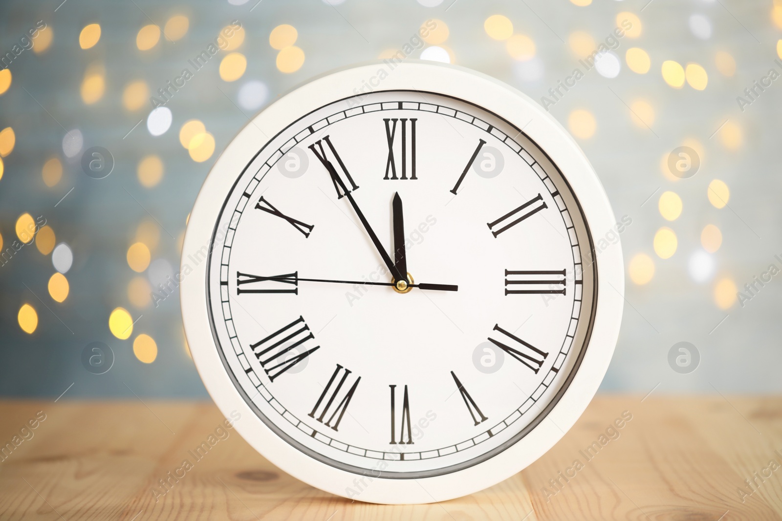 Photo of Clock showing five minutes until midnight on blurred background. New Year countdown