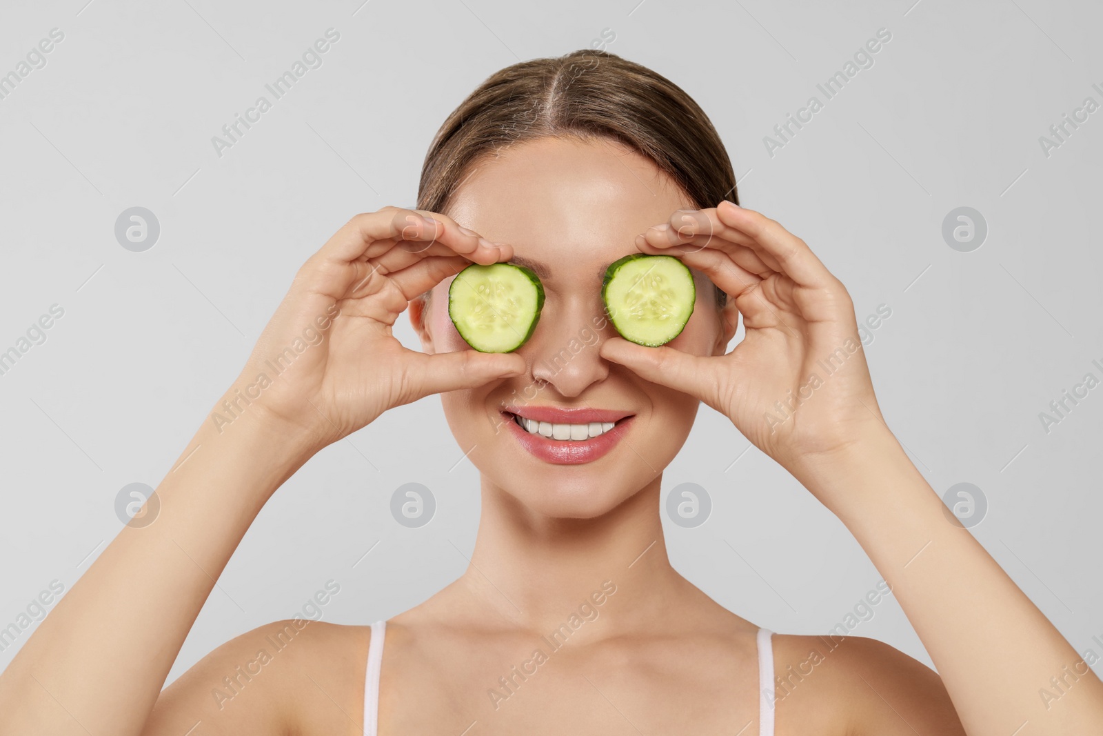 Photo of Young woman with cucumber slices on white background. Eye skin care