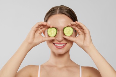 Young woman with cucumber slices on white background. Eye skin care