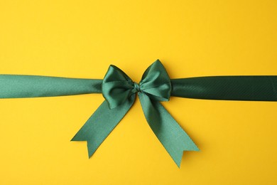 Photo of Green satin ribbon with bow on yellow background, top view