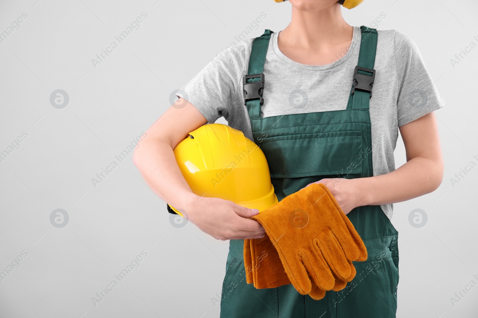 Photo of Female industrial worker in uniform on light background, closeup with space for text. Safety equipment