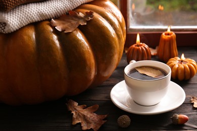 Cup of hot drink and pumpkin shaped candles on wooden table. Cozy autumn atmosphere