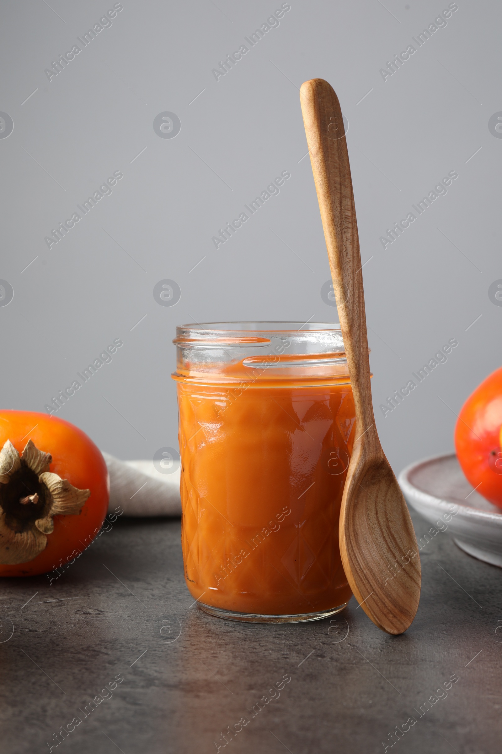Photo of Delicious persimmon jam in glass jar served on gray table